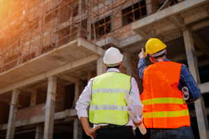 Two construction workers facing a building under construction